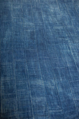 Hand woven indigo denim textile, revealing varied blue hues and textured vertical stripes.