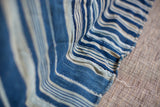 Textured folds of vintage handwoven indigo blue and light striped cotton throw, visible raw edge.