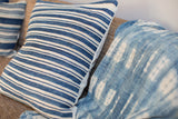 Finely woven indigo striped pillow edge next to textured mudcloth textile with white patterns.