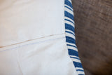 Off-white cotton canvas pillow with unique black and white stitch and blue striped edge.