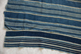 Vintage African indigo textile with varied blue and natural striped panels and visible stitched seams.