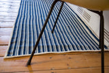 Corner of a vintage hand-woven indigo blue striped runner rug with off-white lines.