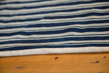 Hand-woven indigo striped textile, revealing its texture and mounted canvas edge.