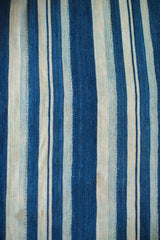 Textural close-up of vintage hand-woven indigo textile, featuring varied blue and cream stripes.
