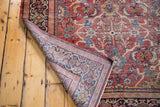 Distressed antique Persian Mahal carpet, folded corner revealing hand-knotted construction beneath the worn rusty orange field.