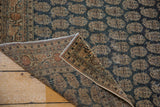 Folded antique Persian Tabriz rug showing secured edge, foundation, and worn charcoal boteh design.