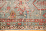 Detail of the antique Serapi rug's secured end, showing exposed knot heads and terra cotta motifs.