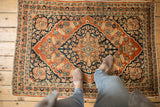Antique Tabriz rug with contrasting rusty orange and navy colors, shown underfoot for scale.