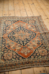 Angled view of an antique Tabriz rug's rusty orange medallion and deep navy floral field.