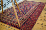 Intricate geometric borders of an antique Turkmen Chuval rug in softened cranberry red and blue.