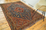 Antique Shiraz rug with serrated geometric medallion, vivid blue field, and storied patina.
