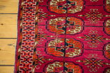 Vintage Turkmen rug, vibrant magenta field, geometric Bokhara pattern, rust, navy, and visible repair.