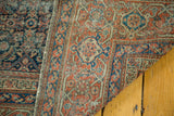 Close detail of distressed antique Fereghan carpet with faded madder red and indigo patterns.