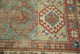 Antique Kazak rug with geometric medallions, a light green field, and distressed texture.
