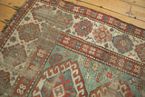 Distressed wide geometric borders and light green field of an antique Kazak rug, foundation showing.