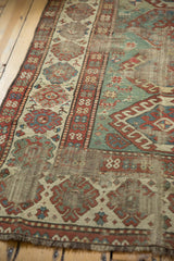 Antique Kazak rug with distressed light green field, wide border, visible foundation, and geometric animal motifs.