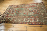 Wide red, ivory, and blue geometric border framing the distressed light green field of an antique Kazak.