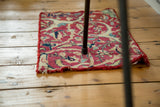 Worn corner of an antique Kerman fragment rug with red binding and ivory botanical pattern.