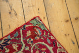 Corner detail of the antique Kerman fragment rug, with time-softened red field and curvilinear green-blue patterns.
