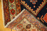 Folded vintage Northwest Persian rug corner revealing indigo field, serrated pattern, and hand-knotted back.