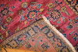 Folded corner of vintage Mohajeran Sarouk rug, showing maroon floral pile and woven foundation.