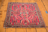 Detailed corner of a vintage cherry red Sarouk rug, showing floral sprays and intricate borders.