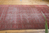 Angled view of an antique Doroksh rug highlighting the distressed texture over its allover vine motif.