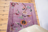Art Deco Nichols rug corner: deep mauve field, banded border, and sprawling floral vines.