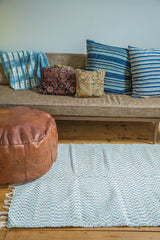 Organic cotton rag rug with colorful flecks and white fringe next to a leather pouf.