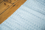 Light blue and white woven texture of organic cotton rag rug with scalloped edge.
