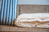Soft off-white organic cotton blanket, rolled to reveal plush texture and ribbed edge.