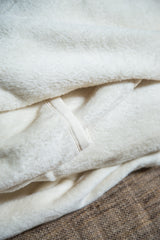 Soft, thick, unbleached organic cotton blanket texture with a visible stitched hem.