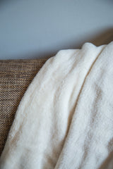 Close-up of the organic cotton blanket, showing its plush, unbleached off-white texture.