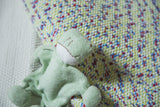 Organic cotton stuffed frog with stitched face, resting on colorful speckled textile.