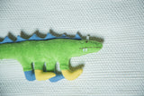 Organic cotton dinosaur toy: green body, blue back spikes, and yellow feet.