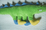 Soft green organic cotton dinosaur body with blue back spikes and yellow, blue feet.