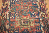 Geometric tribal human and plant forms in red and beige on the indigo field of an antique Caucasian rug.