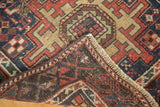 Hand-knotted antique Caucasian rug corner showing geometric pattern, fringe, and overcast edge.