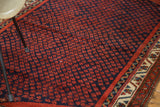 Repeating rust red boteh on navy blue field with multi-color border of a Vintage Persian rug.