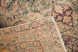 Hand-knotted weave and fringe of an antique Kerman rug, with beige, blue, red floral pile.