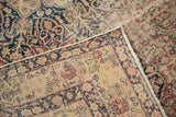 Antique Kerman rug folded to show hand-knotted pile, fringe, and classic floral border.