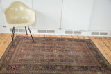 Antique Tabriz rug corner with herati motif, navy border, and distressed wool pile.