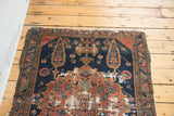 Distressed upper corner of antique Malayer rug with navy and red geometric pattern, frayed edges.