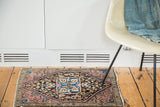 Styled lifestyle view of an antique Farahan Sarouk mat with a plum and blue floral medallion, measures 1'11