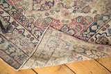 Antique Kerman rug's folded corner reveals hand-knotted construction, floral motifs, and secured edges.