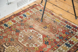 Distressed geometric shield motifs with wine red and saffron tones on an antique Caucasian rug.