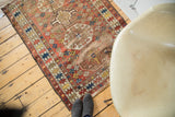 Antique Caucasian rug showing distressed geometric tribal patterns in wine red and saffron with aged ends.