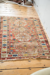 Distressed antique Caucasian tribal rug in wine red, saffron, blue, showing tattered ends.