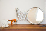 Vintage barber mirror featuring a round aged glass, accordion arm, and fleur de lis bracket.