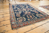 Aged fringe, blush rose palmette border, and dark blue floral antique Mohajeran Sarouk rug.